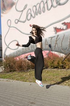young attractive woman in hip hop dress dancing and jumping in urban background