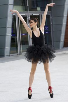 beautiful young ballet dancer in black tutu dancing outside in a modern city