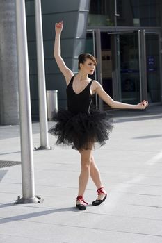 beautiful young ballerina in black tutu taking a classic ballet pose outdoor near a moder building