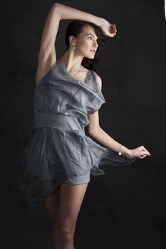 portrait of trendy young woman in elegant blue dress posing against black background