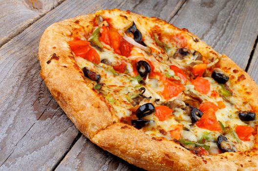 Freshly Baked Vegetarian Pizza with Tomatoes, Black Olives and Cheese closeup on Rustic Wooden background