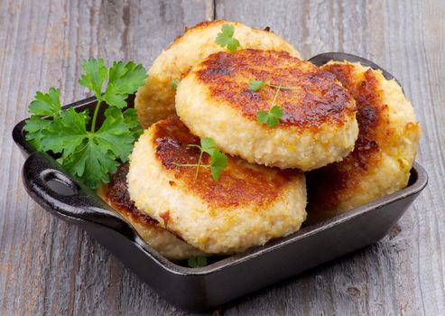 Delicious Chicken Meat Cutlets in Black Saucepan with Parsley isolated on Rustic Wooden background
