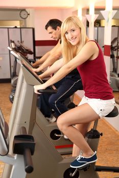 A handsome man and an attractive woman working out on a bicycle in a fitness center