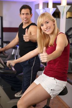 A handsome man and an attractive woman working out on a bicycle in a fitness center
