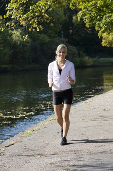 Pretty young blond girl running in the park near river
