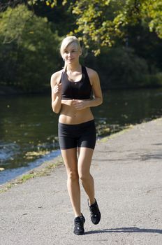 cute blond girl running in the park near river in sportwear