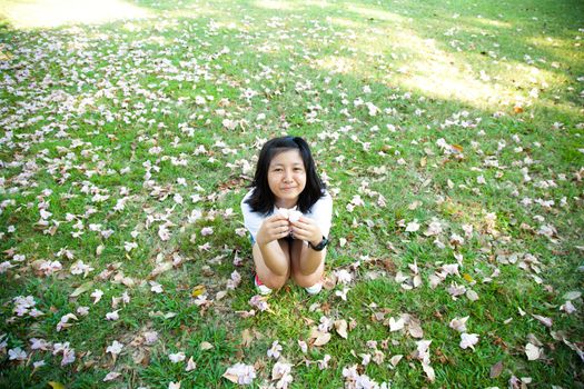 Teenage girl sitting on grass Hands holding flowers. And the blossoms filled the lawn in the park.