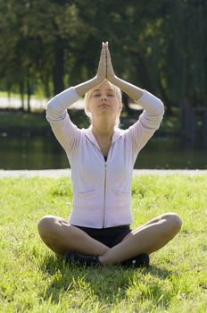 young woman in meditation pose on the grass in a park in backlight