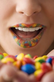 close up on woman mouth with colored lips an color candy in hand