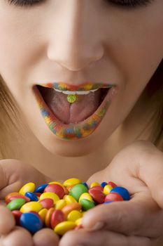 close up of colored open mouth of girl with color smarties in hand