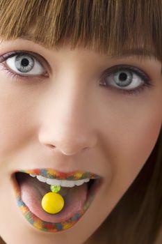 close up of young girl with multicolor lips and a yellow candy on her tongue