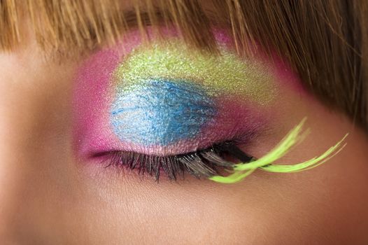 eye close up with colored make up and green long eyelashes