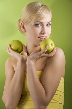 very cute blond girl with yellow top and green apple looking in camera