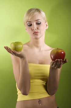 blond girl with red and green apple in act to take a decision of what kind of apple to eat red or green