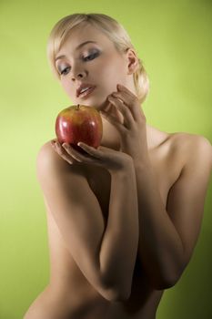 fashion and glamour shot of a dreaming nude young woman with red apple on green background