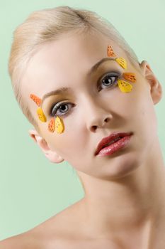 portrait of pretty and young blond woman with colored creative make up on green background