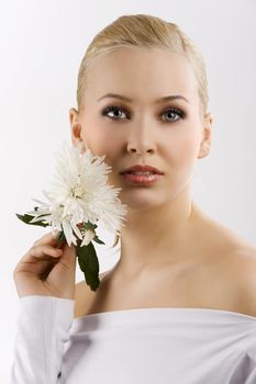 beauty portrait of young cute blond girl with white top and some flowers near face