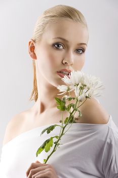 beauty portrait of young cute blond girl with white top and some flowers near face