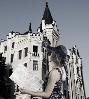 elegant woman in blue polka dot dress and hat looking at a tourist map