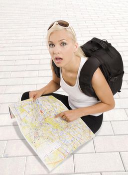 pretty girl in vacation with backpack sitting down with map and looking in camera surprised