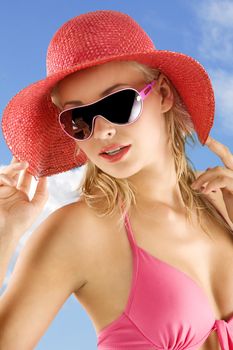 closeup portrait of pretty blond woman wearing a nice summer red hat and sunglasses against a blue sky