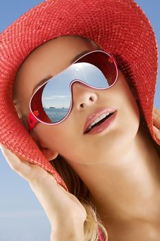 fine portrait of young cute woman with red summer hat and sun glasses looking at the sea in a sunny day