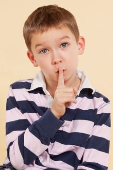 The secret.  Don't tell anyone. Young boy with finger over his mouth isolated on neutral background. Facial expressions concept. Psst