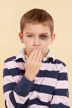 Young boy with black eye and hand over his mouth isolated. Domestic violence concept. Psst