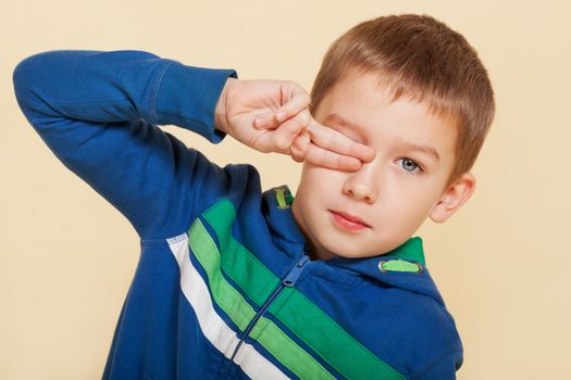 Young cute boy ten years old covering his eye and looking into the camera isolated. Youth fashion concept.