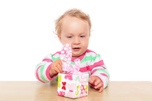 Cute one year old blonde baby girl with blue eyes playing with colorful present isolated on white background. Christmas and birthday giving present concept.