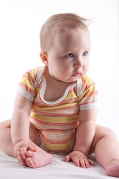 Beautiful cute baby girl with big shiny eyes sitting and looking isolated on white background.