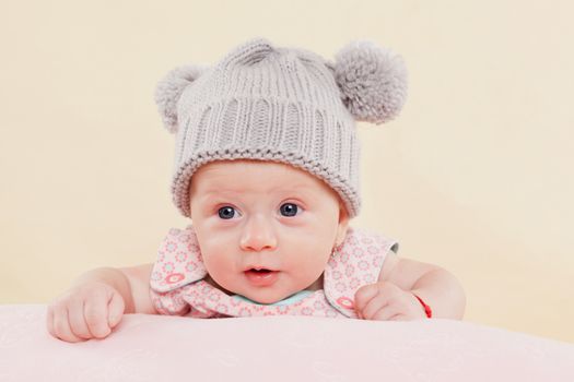 Beautiful cute surprised baby girl with grey cap lying on blanket faced into the camera. 