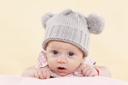 Surprised baby girl with grey hat looking into the camera isolated on neutral background. Cute newborn concept.