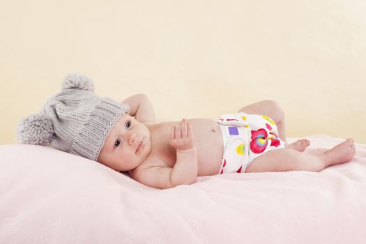 Happy naked baby with colorful diaper lying on bed and relaxing. Cute newborn baby girl.