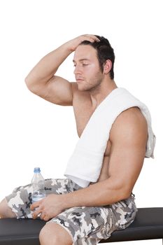 Bodybuilder resting after workout sitting on bench with water and towel isolated on white background. Sport, Fitness and Health.