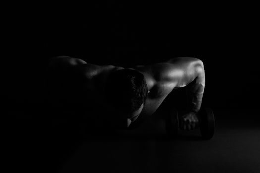 Caucasian bodybuilder performing push ups isolated on black background. Fitness fine art portrait.