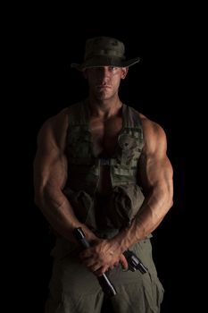 Serious young muscular soldier with gun and flashlight in green uniform standing proud isolated on black background. Army, security and protection.