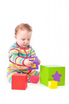 Cute one year old baby girl in colorful clothing playing with colorful blocks isolated on white background. Creativity and development concept.