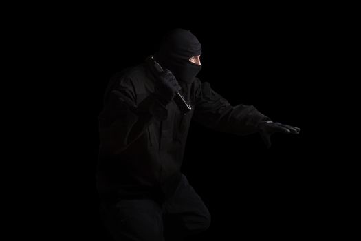 Man in black mask and black cloth holding flashlight isolated on black background. Dangerous criminal committing crime.