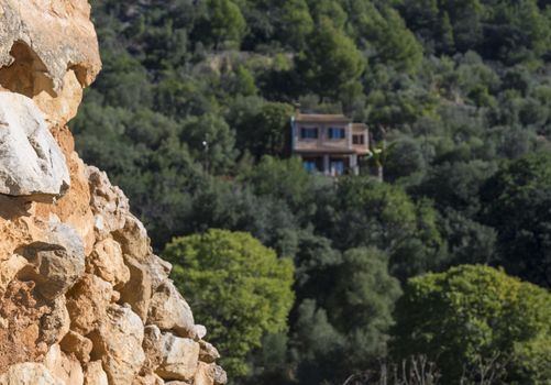 Mountain side with loose, red, limestone rocks and house in the forest out of focus. Mallorca, Balearic islands, Spain.