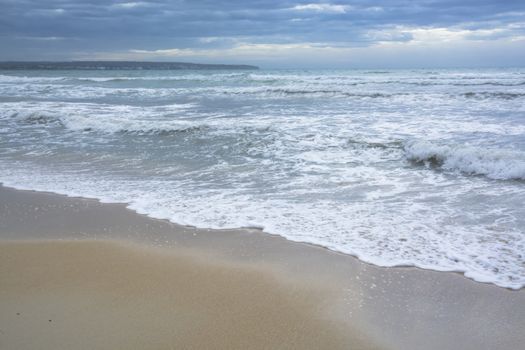 Mediterranean blues in autumn. Sandy beach and storm waves in November, Mallorca, Balearic islands, Spain.