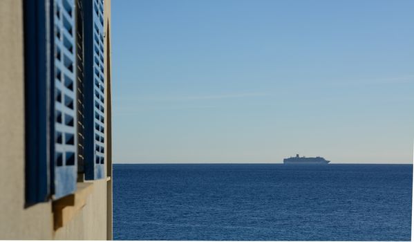 Passenger ferry boat on horizon and window shutters in the forefront.