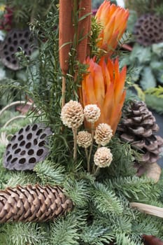 Decorative autumnal flower arrangement with cones and spruce twigs in oranges and green, vertical image.