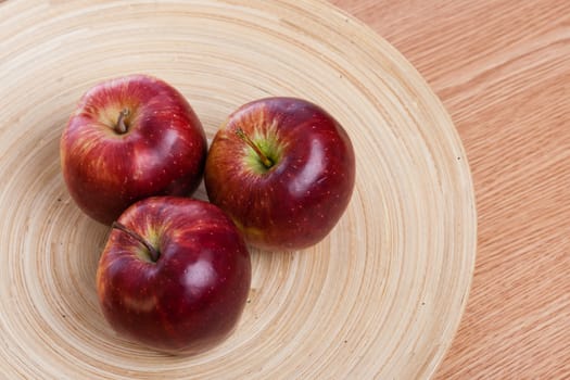 three red apples on a wooden plate