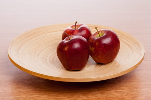 three red apples on a wooden plate