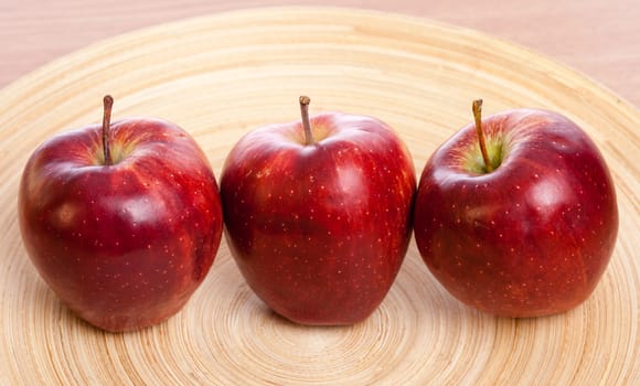 three red apples on a wooden plate