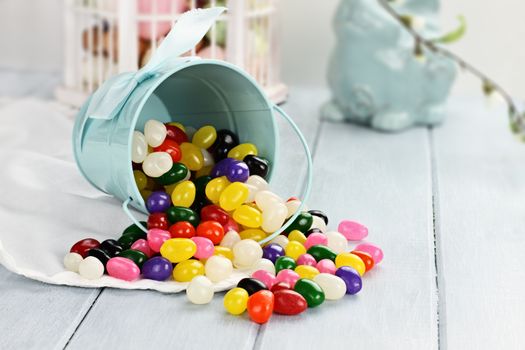 A blue tin bucket tipped over, spilling jelly beans onto a table. Shallow depth of field.