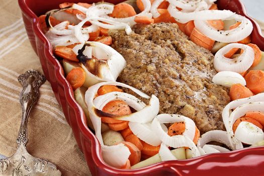 Casserole dish of freshly prepared meatloaf with onions, carrots and potatoes. Shallow depth of field.