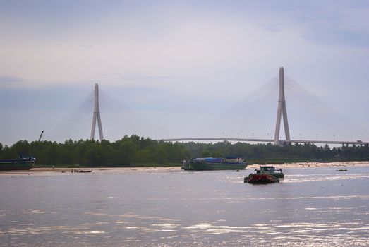 The Can Tho suspension bridge is the bridge with the longest main span in Southeast Asia. Built by the Japanese. Seen from Can Tho City. One large barge is stranded on a sandbank but a smaller barge continues its way on the Hau River.