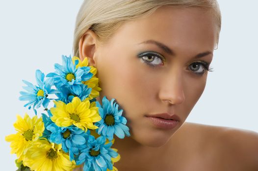 beauty portrait of pretty young blond girl with blue and yellow daisy near her face